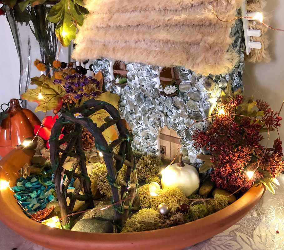 Fall themed indoor fairy garden with handcrafted English cottage lit with fairy lights.