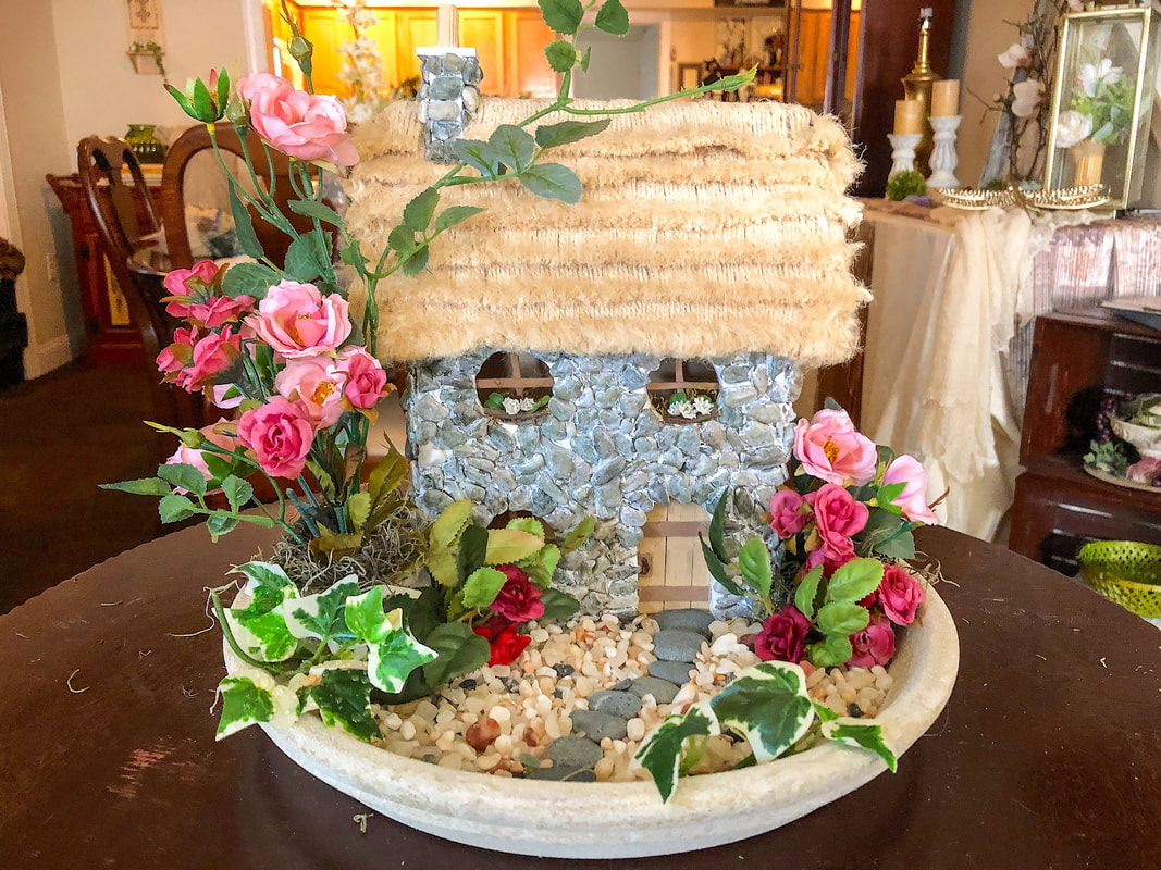 Handcrafted fairy cottage with mini faux spring roses on a terra cotta plate.