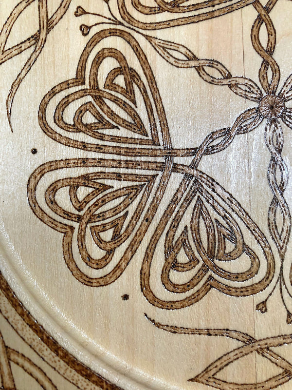 Closeup of shamrock detail on a hand drawn wood burned decorative plate.