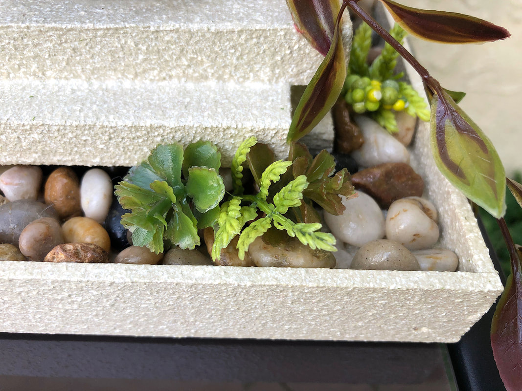 Closeup of river rocks and faux greenery on a handcrafted candleholder by Di's Studio Designs.