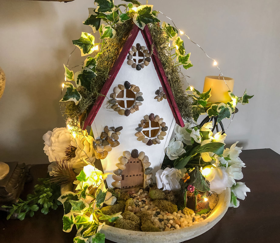 Indoor fairy garden with handcrafted fairy cottage and faux florals.