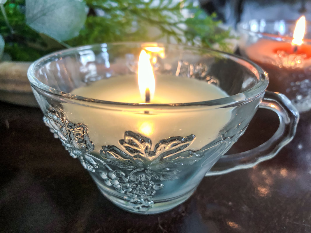 Homemade green soy candle burning in a glass tea cup.