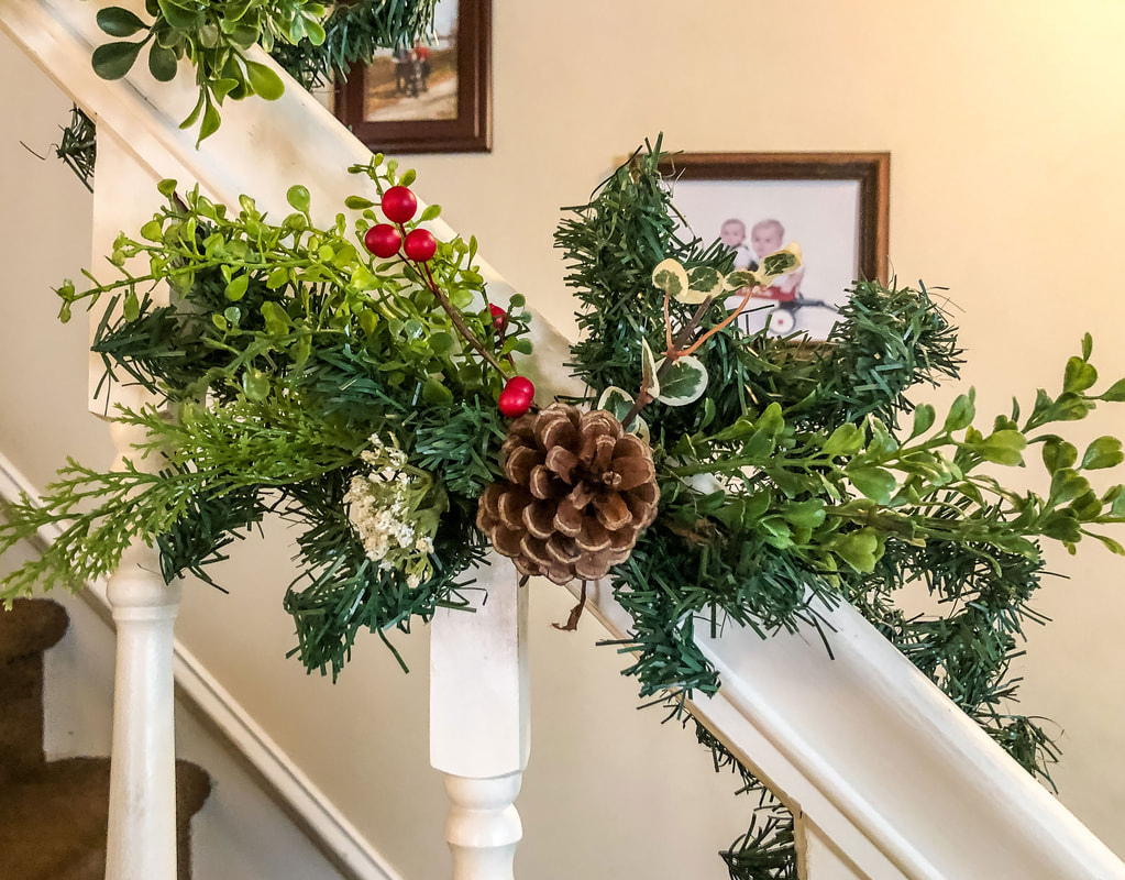 Railing wrapped with faux garland, greens, red berries and a pinecone. 