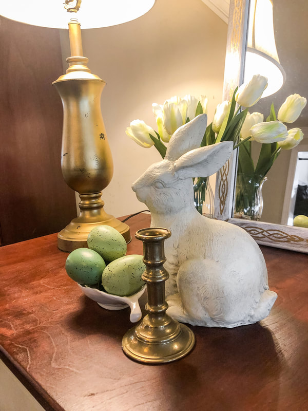 Small vignette with white Easter bunny, green pastel eggs and a gold candlestick.
