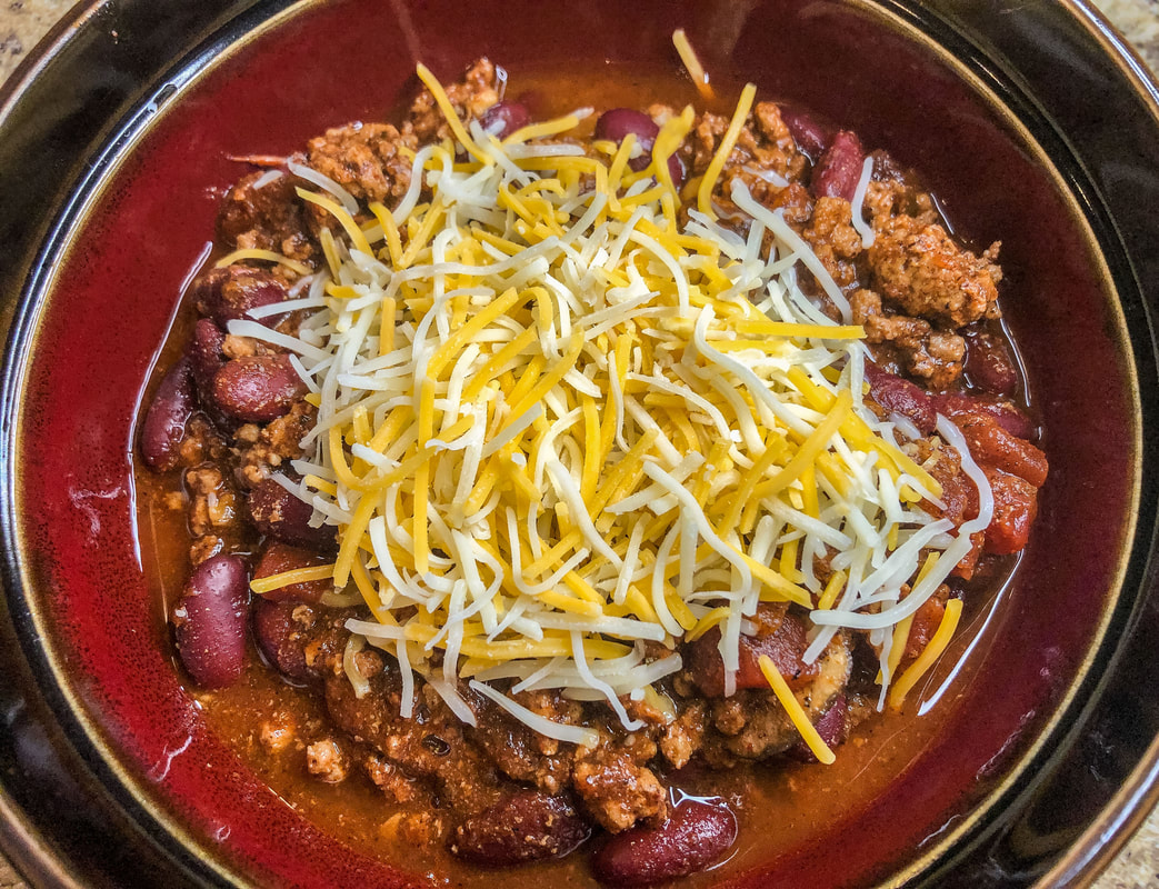 Bowl of homemade chili with shredded cheese on top.