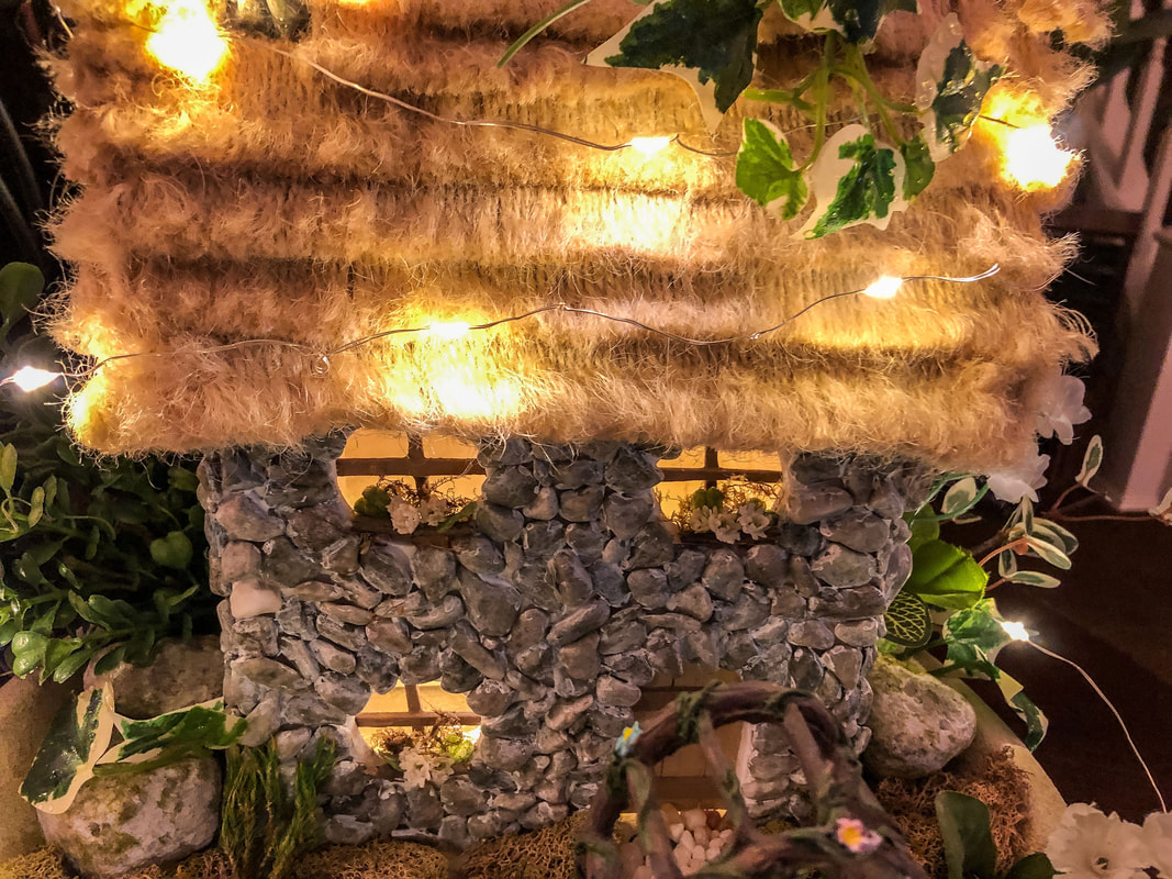 Handcrafted thatched fairy cottage with fairy light strands.