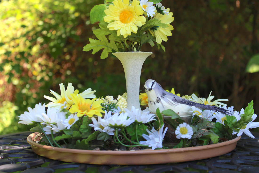 Faux floral arrangement with bird and repurposed vase and plate.