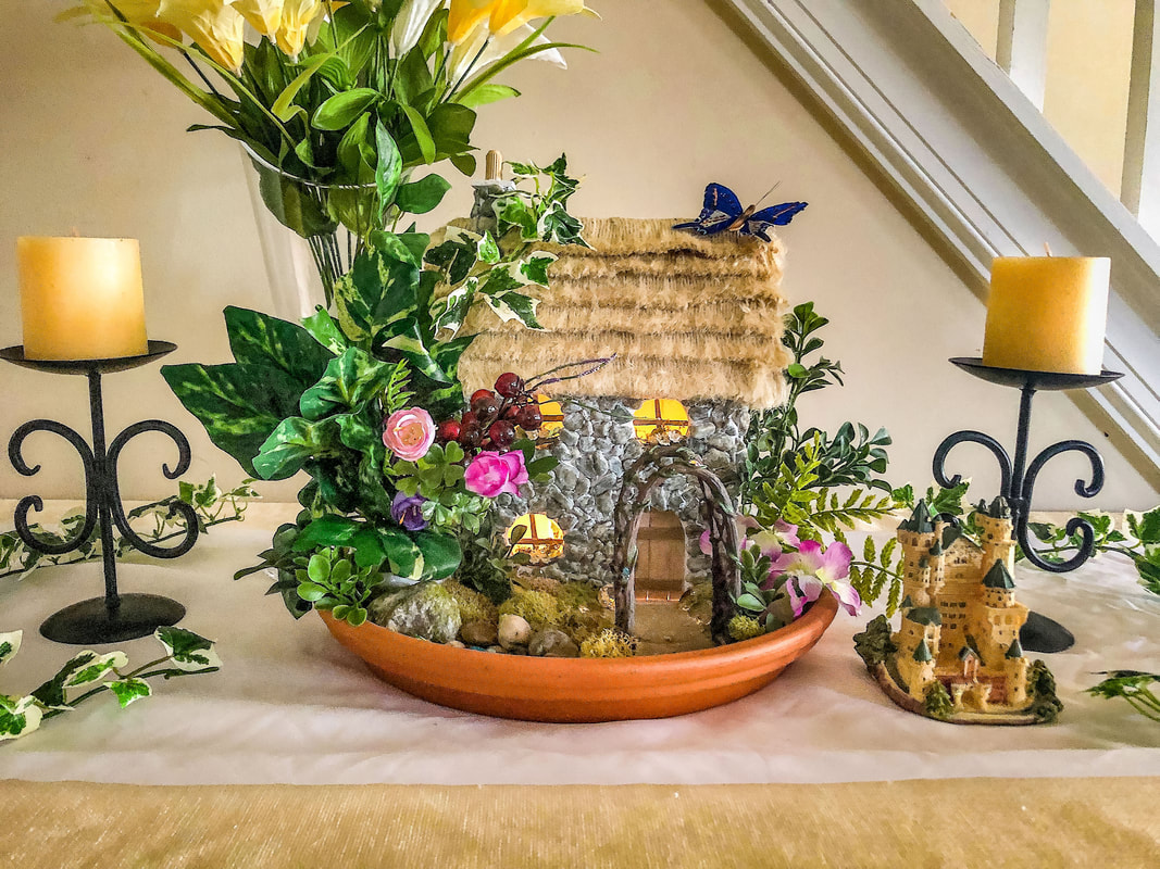 Indoor fairy garden with faux florals featuring a handcrafted miniature English Cottage.