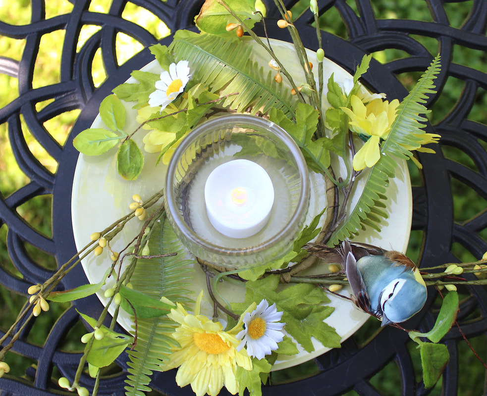 Top down view of a DIY candleholder with faux florals, bird and repurposed dish and glass.