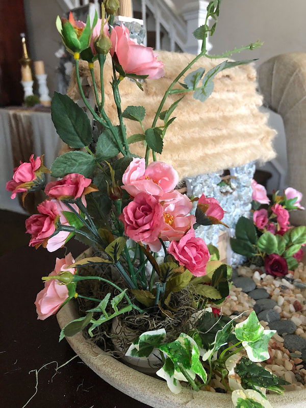 Miniature pink faux roses and ivy in an indoor fairy garden.