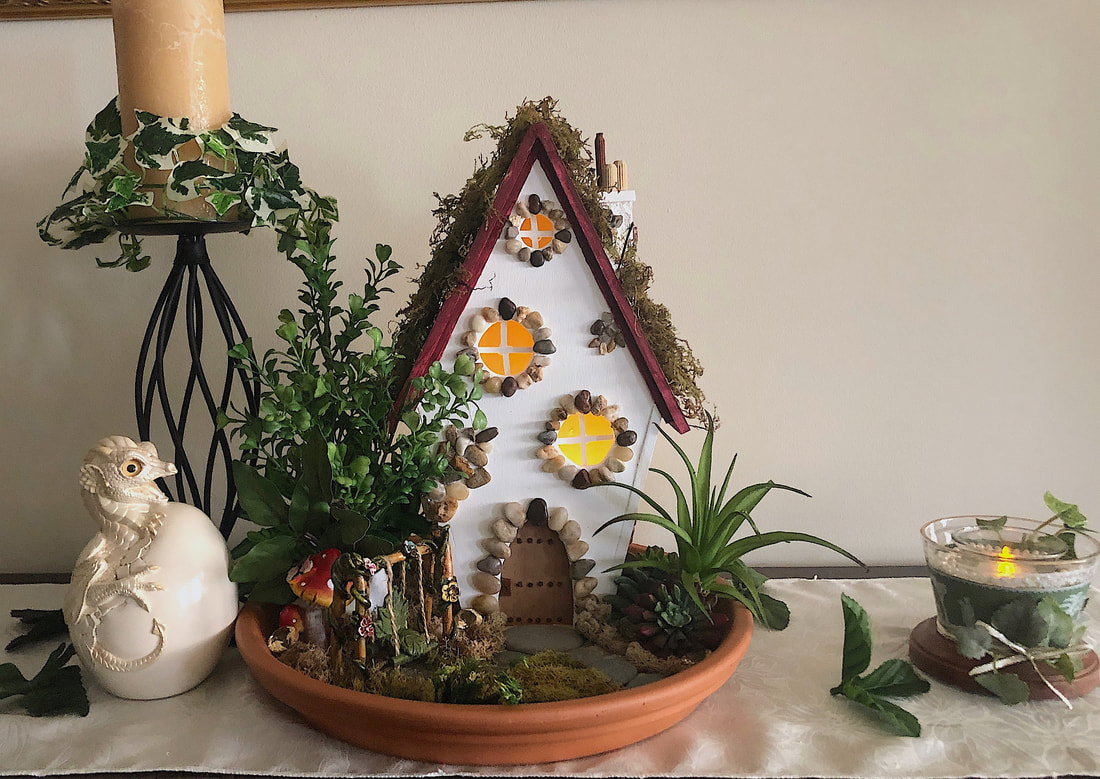 Vignette featuring a handcrafted indoor Fairy Cottage with faux floral garden.
