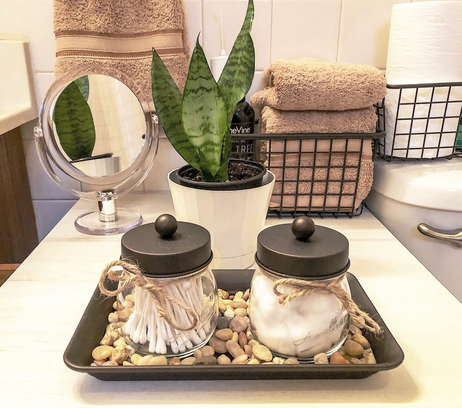 Vignette in bathroom with apothecary jars, river rocks, taupe hand towels, and a snake plant.