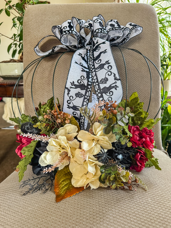 Pumpkin wireframe wreath with black cat ribbon and red, cream, and black faux florals