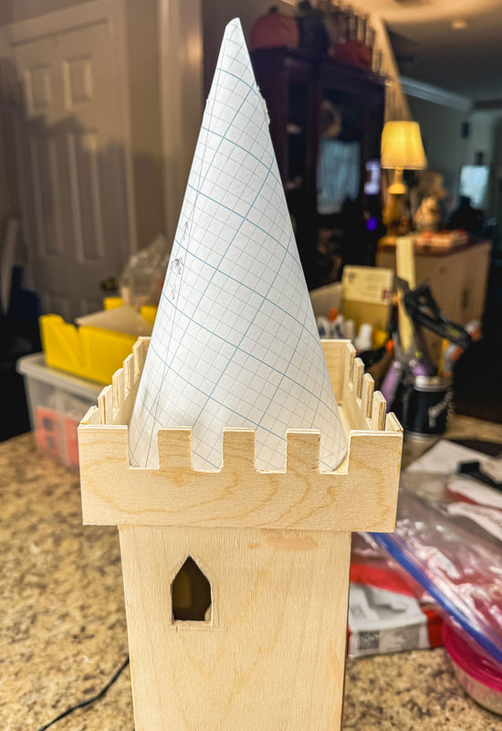 Paper cutout cone made from grid paper set atop a wooden castle tower.