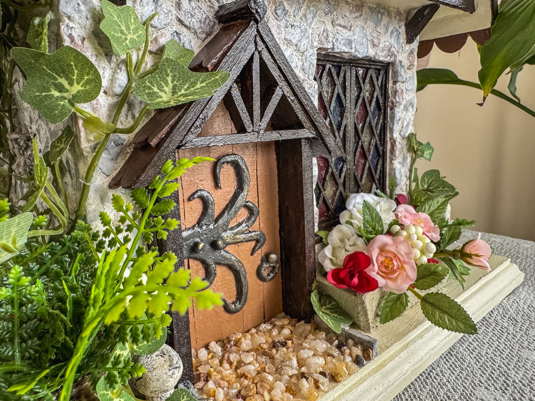 Closeup of the front facade of a handcrafted fairy house with faux florals.